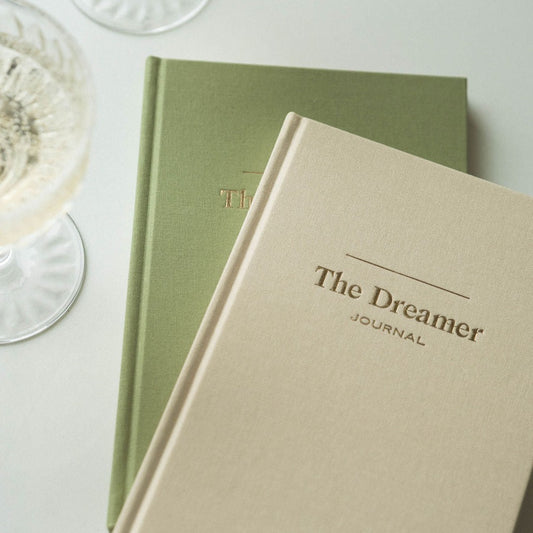 Dream Daily Dreamer Journals in Champagne and Matcha next to glasses of Champagne